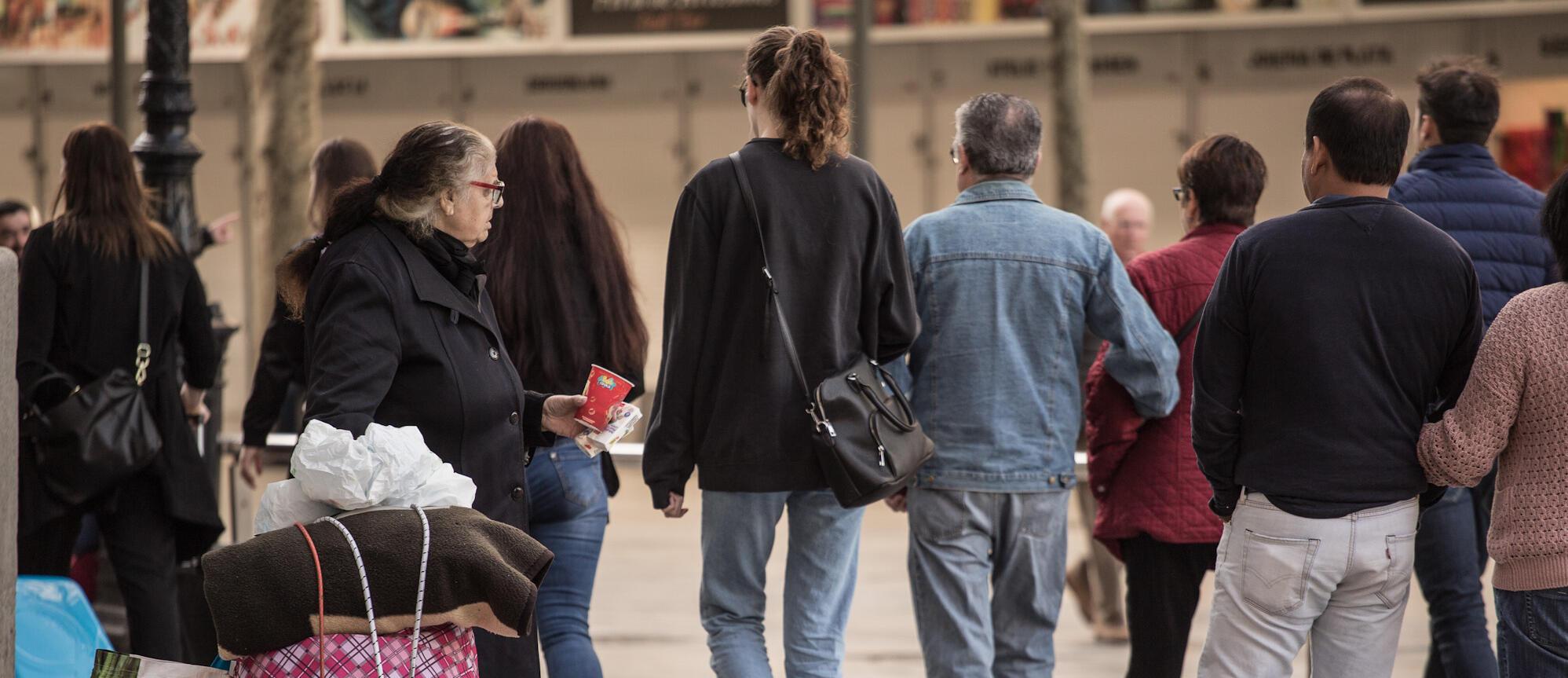 Fotografia persona demanant almoina al carrer, i altres persones caminant